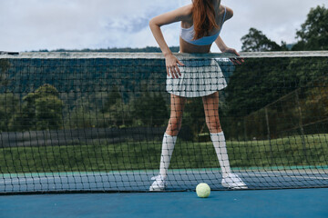 Female tennis player leaning against the net in a sporty outfit, showcasing determination and...