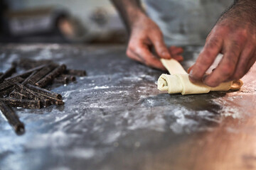 Baker's hands rolling croissant dough with chocolate sticks on floured table