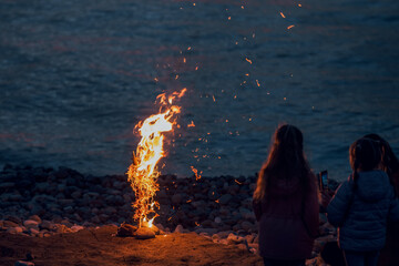 Sea night breeze and flame. Friendly evening by the fire. People or kids girls sitting around a campfire. burns with bright sparks brightly, illuminating them and the surrounding landscape, warm light