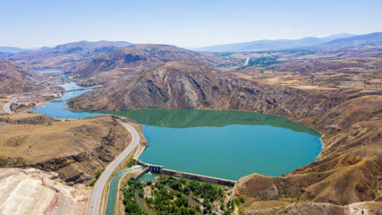 Aerial view of dam lake surrounded by mountains and curving roads