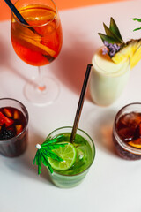 A vibrant collection of Negroni, Aperol Spritz, Mojito, Sangria, and Pina Colada cocktails on a white, peach, and blue backdrop. Fresh fruit garnishes and sharp lighting enhance their summer vibes
