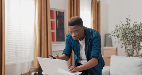 A young adult in his new flat drinks coffee, stands on boxes, and clicks through furniture...