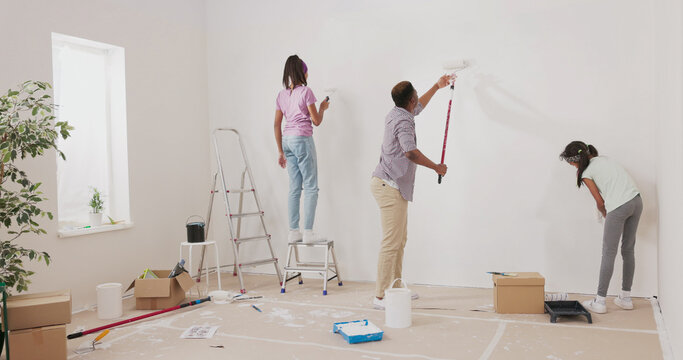 A family renovation project unfolds as a father and his daughters paint their apartment. With white paint rollers in hand, they work together on the walls, and the daughter climbs a ladder to assist