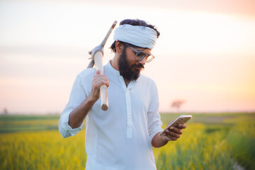 A Pakistani Indian farmer in traditional white attire, holding a hoe on his shoulder while using a...