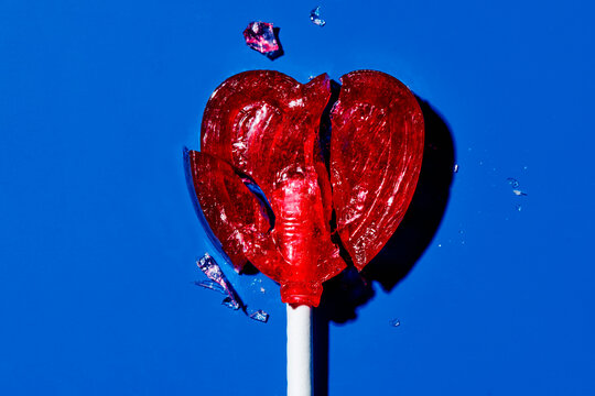 Broken heart-shaped lollipop on a blue background symbolizing heartbreak