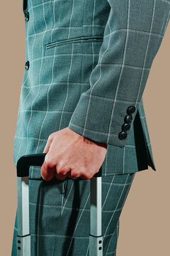 Businessman in gray suit holding trolley suitcase against brown background