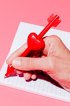Man writing a love letter with a heart and arrow shaped pen on a notebook