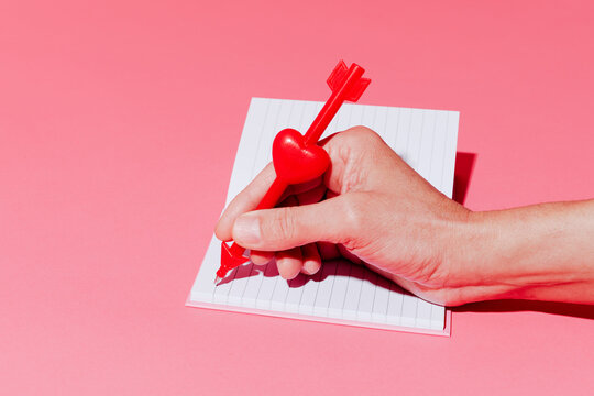 Man writing a love letter with a heart and arrow shaped pen in a studio setting