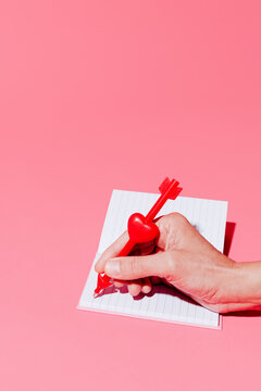 Man writing a love letter with a heart and arrow shaped pen in a studio setting