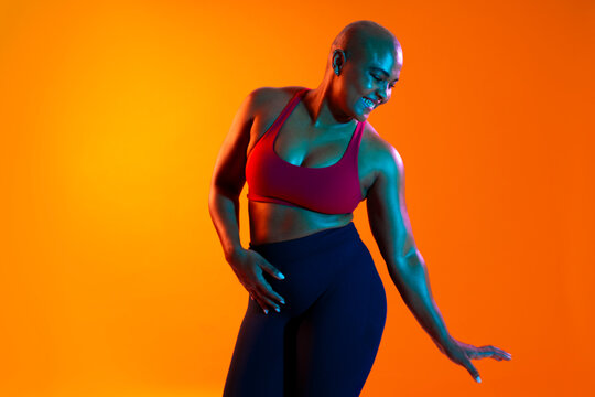 Bald woman in sportswear dancing in a studio with an orange background