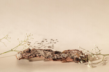 Natural bark podium with gypsophila and shadow on a light beige background.
