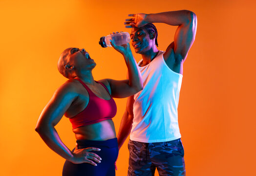 Athletes in sportswear hydrating during a workout on an orange background