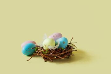 Painted eggs and feathers in a nest on a light yellow background.