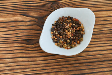 Mix of peppercorns in a bowl on a wooden background.