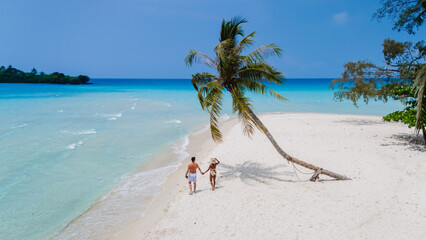 A lovely couple enjoys quality time on the stunning beaches of Koh Kood Island, Thailand, surrounded by azure waters and a tall palm tree, embodying a perfect tropical vacation