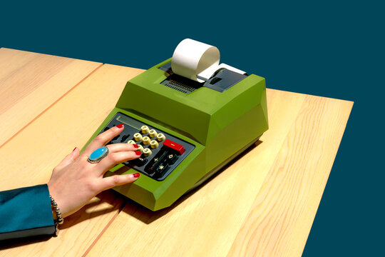 Retro mechanical calculator on a wooden desk with a hand wearing a ring