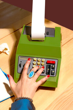 Hand with red nails using a vintage mechanical calculator on a wooden desk