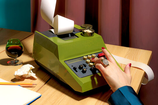 A female hand using a vintage calculator on a desk with a glass of wine and office supplies