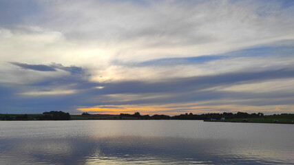 Obraz premium The perfect sunset moment over a rural lake, with still water mirroring the last rays of daylight in the evening