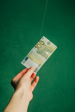 A hand holding a 100 euro bill on a hook against a green background