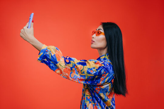 Woman taking a selfie with a smartphone against a red background