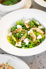 Fresh salad with arugula, sliced pears, goat cheese, and pumpkin seeds served in a white bowl. A healthy and vibrant dish perfect for a nutritious meal or appetizer.