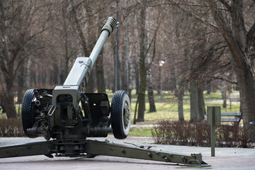 A large artillery piece stands prominently in a park, surrounded by bare trees. The overcast sky...