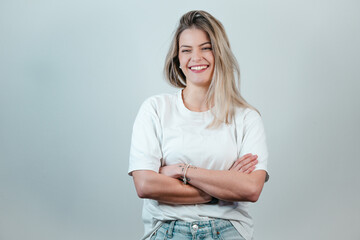 Young blonde German woman in a white T-shirt, posing with crossed arms in front of a plain white...