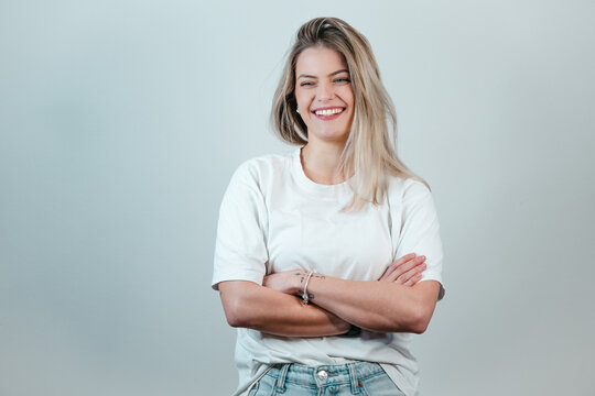 Young blonde German woman in a white T-shirt, posing with crossed arms in front of a plain white backdrop