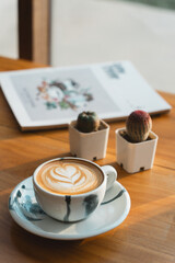 A latte and potted succulents on a wooden table alongside a minimalist white-cover magazine, radiating cozy charm.