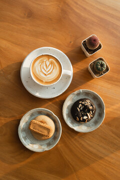 A latte with foam art, paired with soft-baked cookies and succulents, on a cozy wooden table.