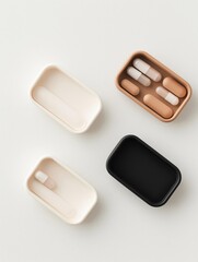 Four rectangular pill cases in different colors - white, beige, and black. the cases are arranged in a horizontal line on a white background.
