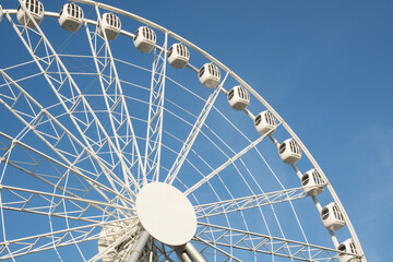 Part of white Ferris wheel against blue sky on cloudless summer day. Outdoors. Amusement park.