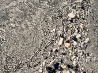 assorted pebbles and sand under clear shallow water with sunlight ripples. natural abstract texture. eco design, travel themes, relaxing nature