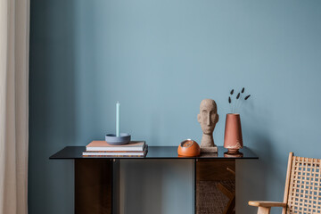 Modern console table with pastel candle, abstract head sculpture, and terracotta vase against blue...