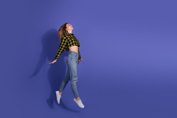 Young woman jumping gracefully against a purple background wearing a checkered shirt and casual...