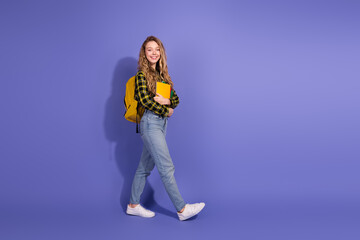 Smiling young woman holding books and walking on a purple background