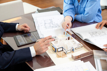 Residential sales: Owner and salesman discussing while looking at design drawings, hands, no faces