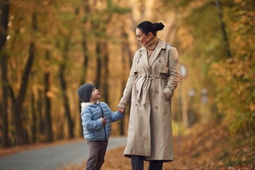 Fototapeta premium Mother with her son are having a walk in autumn forest near the road