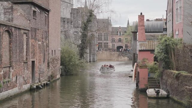 Barca con turisti che naviga attraverso un canale della citt&agrave; di Gent, citt&agrave; Europea, durante una giornata nuvolosa. Boat Tour.