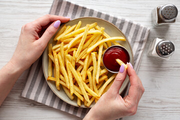 Woman dipping French Fries into Ketchup, overhead view.