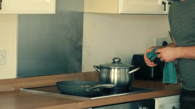 Lifting hot pot with towel from stove. Holding steaming saucepan with covered lid. Carrying freshly cooked noodles in metal pot. Removing boiling container from induction cooktop