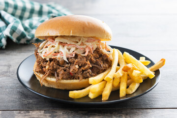 Pulled pork sandwich with coleslaw salad and french fries on wooen table
