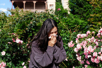 Woman suffering from seasonal allergies, holding a tissue to her nose. Hay fever, pollen allergy,...