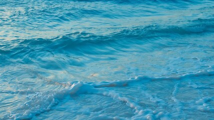 Obraz premium Close-up view of turquoise waves gently lapping the shore, capturing the vibrant blue tones and foamy white crests.