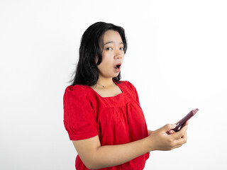 Naklejka premium A studio portrait of a young beautiful Indonesian Asian woman in a casual red shirt looks happy while typing on her phone. isolated on white background