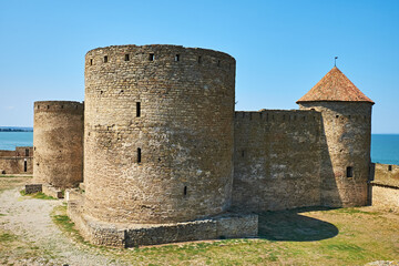 Ancient medieval fortress with massive stone towers near the sea under a clear blue sky.