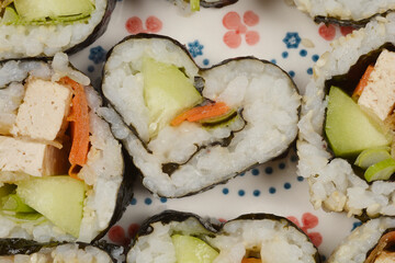 A close-up, top-down shot of a heart-shaped sushi roll amidst other sushi pieces on a decorative plate