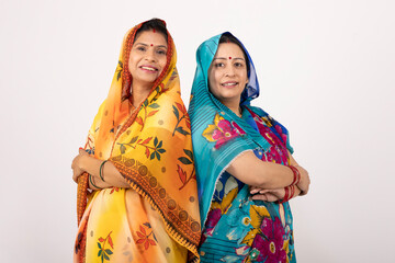 Mid shot of two Indian happy rural young women arm crossed while looking at the camera on grey...