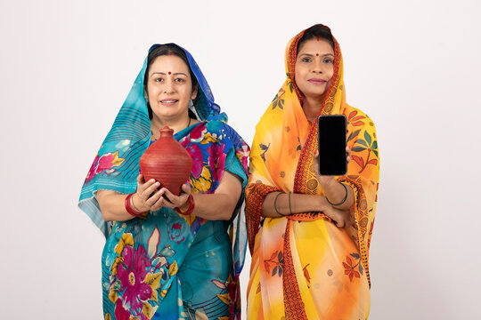 Indian happy rural women holding piggy bank and smartphone screen isolated on grey studio background - Powered by Adobe